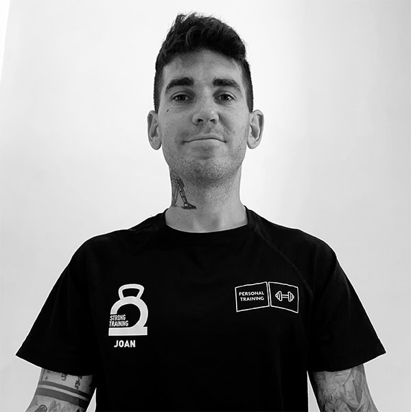Una persona con una camiseta negra con logotipos de gimnasio mira con confianza hacia adelante, encarnando la esencia de un entrenamiento fuerte.